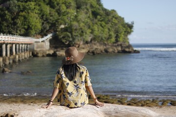 Woman with hats on sandy beach near sea, back view