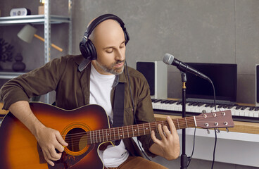 Middle-aged Caucasian man artist in earphones play guitar record song. Young male singer in...