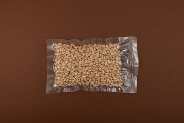 Pine nuts in transparent vacuum package on brown background, close-up. Cedar nuts. Top view, copy...