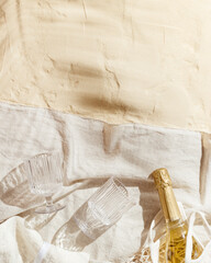 Summer pastel background with trendy wine glasses, bottle sparkling wine in mesh bag on beige beach...