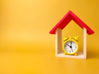 Toy house and alarm clock isolated on yellow background with copy space
