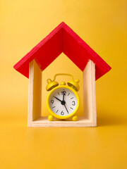 Toy house and alarm clock isolated on yellow background.