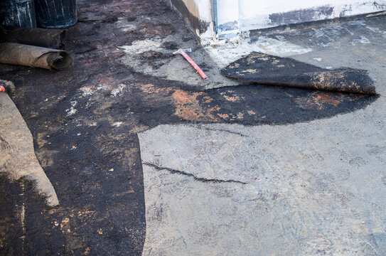 Workers remove the deteriorated bituminous sheath attached to the floor of a building's terrace. Then a new waterproofing layer will be placed.