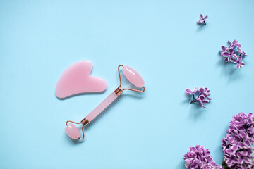 A pink facial massage kit lies on a blue background. Lilac flowers