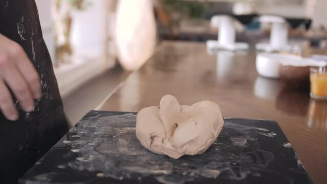 Female hands crumple and roll out piece of clay on table, front view, closeup. Potter prepares clay for processing on table.