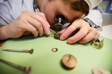 Close-up of concentrated engineer of wristwatch factory wearing monocular magnifying glass using...