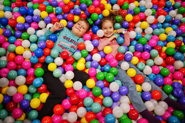 Fototapeta na wymiar Brother with sister playing in colorful ball pit. Day care indoor playground. Balls pool for children. Kindergarten or preschool play room.