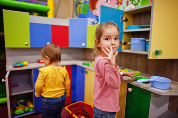 Cute sisters playing in indoor play center. Kindergarten or preschool play room. In the children's kitchen.