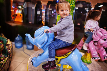 Two sisters rides an elephant carousel in fun children center.
