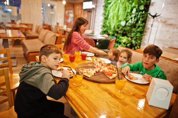 Mother with four childrens eat pizza in pizzeria.