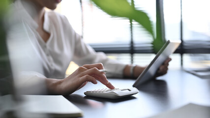 Naklejka premium Cropped shot businesswomen using a calculator and digital tablet at office desk. Financial and investment concept