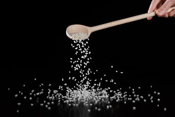 White round rice is poured from a wooden spoon onto the table. Selective focus. Black background.