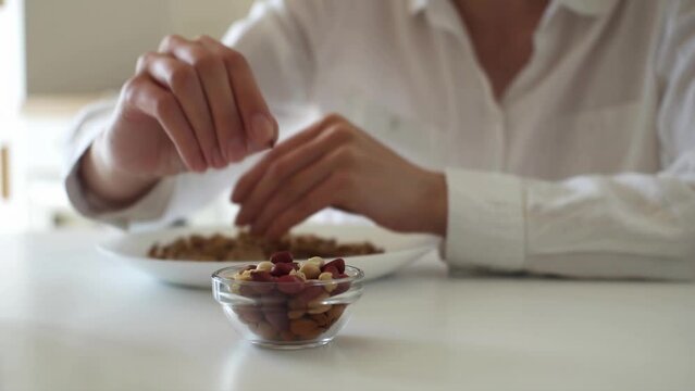 Close-up girl's hands are peeling peanuts. Peanut shelling. Nuts in a plate a white race girl sits at the kitchen table eats nuts with pleasure without having an allergic reaction to peanuts
