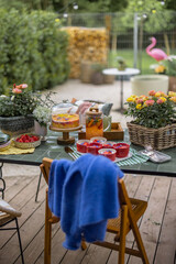 Beautiful backyard with festively served dinner table on a terrace during summer time, wooden chair with blue sweater in front