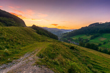 Obraz premium mountainous countryside landscape at dawn. rural fields on the hills. village in the distant valley. gorgeous sky with clouds glowing in morning light