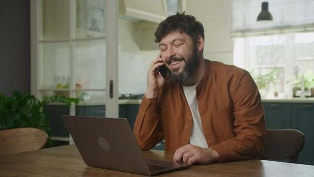 Peforming a sale on his phone in front of a laptop computer. Man recieving good news on phone