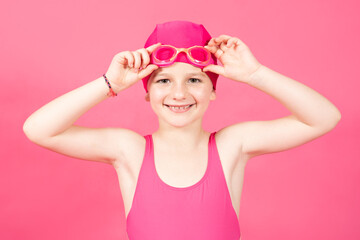 Cheerful cute swimmer looking at camera isolated on vivid pink background. Little girl prepared to...