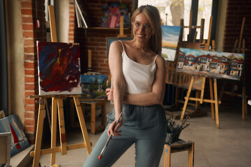 Portrait of a talented female artist working on a modern abstract oil painting, gesturing in broad...