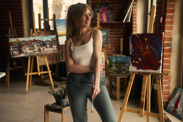 Portrait of a talented female artist working on a modern abstract oil painting, gesturing in broad...