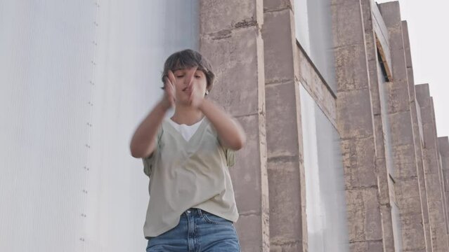 Medium shot of energetic young short haired girl looking at camera while dancing waacking style outdoors in summer
