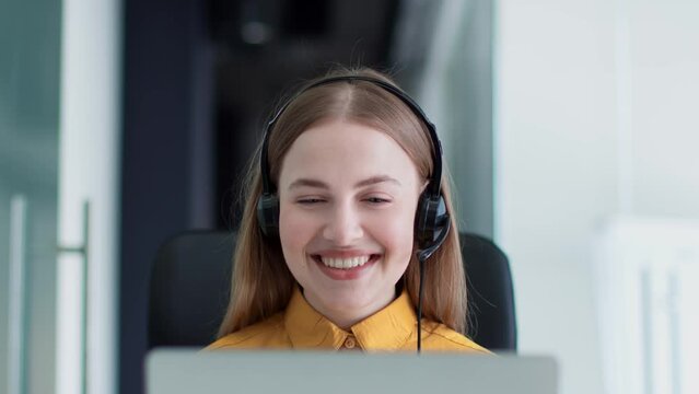Online consultation. Close up portrait of young woman manager wearing headset video chatting with client via laptop