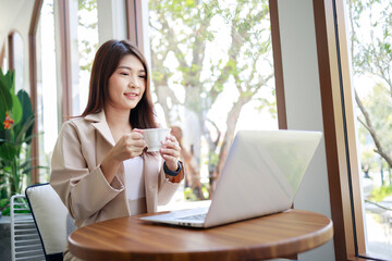 Asian businesswoman in casual suit drinking coffee and working by laptop in the coffee shop