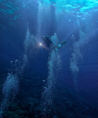 Underwater photography of a scuba diver in the deep blue sea in beautiful light and surrounded by air bubbles.