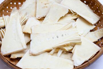 Sliced raw bamboo shoots in bamboo basket on white background.