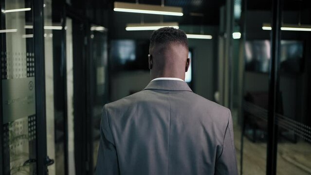 The camera follows the back of a man walking down the corridor of a business center