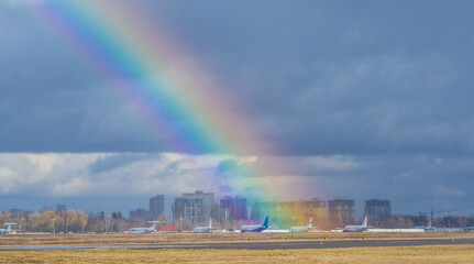 A huge rainbow falls on passenger airliners parked in the parking lot in the summer. Rainbow over the airport, bright future, planes and joy