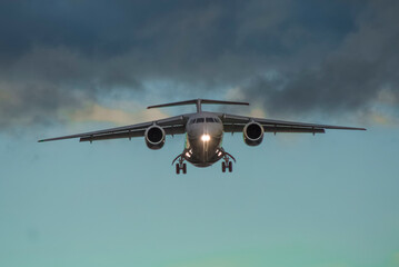 A civilian jet comes in to land at an airport at sunset with landing gear extended and landing lights on, front photo