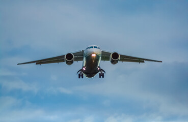 A civilian jet comes in to land at an airport at sunset with landing gear extended and landing lights on, front photo