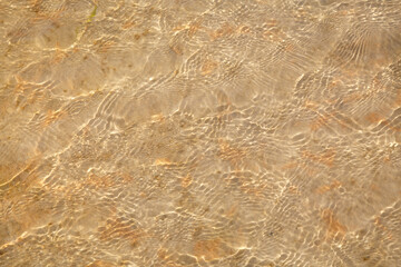 Natural wallpaper, water surface with light ripples and a sandy bottom under clear water.