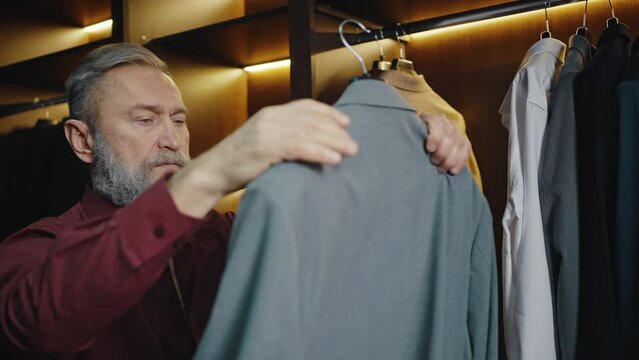 Morning dressing. Bearded mature businessman choosing jacket at wardrobe, getting ready for going to office, free space