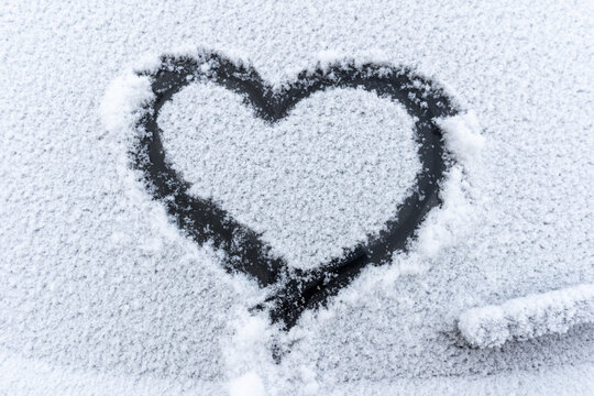 Snow heart on the car window with copy space. Heart sign in fresh snowflakes. Heart shape symbol drawn on snowed car glass. Love concept. Valentine's Day. Declaration of love