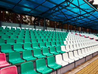 Obraz premium Empty stadium stands, open-air stadium, for football and athletics, plastic seats of different colors under a blue canopy
