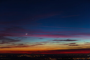 Crescent young Moon and planets on colorful sky.