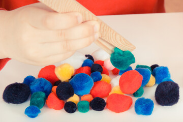 Preschooler playing with small pompoms and wooden tongs. Development of kids motor skills, coordination and logical thinking