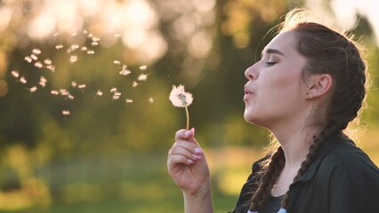 A young girl gently looks at the dandelion flower and blows it away.