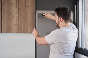 Young hispanic man installing furniture in the kitchen using a screwdriver. Assembling modern kitchen furniture.