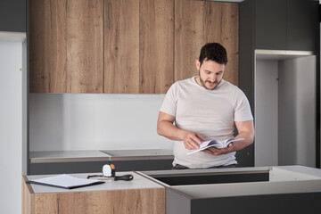 Young argentinian man reading instruction manual before installing furniture on modern new kitchen.