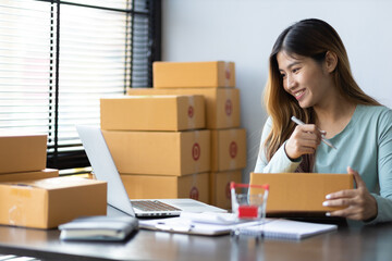 Woman running a small startup business in an office is working on a laptop and boxes for packing and preparing items for shipping.