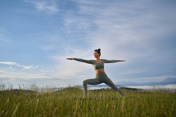 Fototapeta na wymiar Charming woman in sport clothes doing yoga exercises among summer mountains. Pretty dark haired lady enjoying morning workout on fresh air.