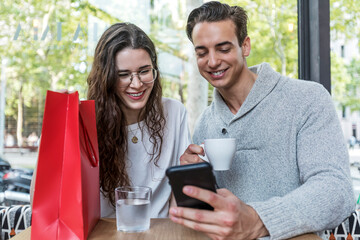 Smiling couple at cafe using mobile phone