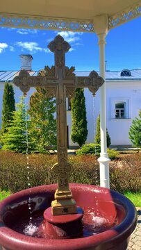 Horizontal video, in a large red bowl there is a large golden Orthodox cross, from which water flows. High quality FullHD footage