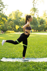 Fototapeta premium a girl outdoors in the park goes in for sports in a sports purple top in black leggings on a blue sports mat in the background a meadow and trees