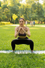 a girl outdoors in the park goes in for sports in a sports purple top in black leggings on a blue sports mat in the background a meadow and trees