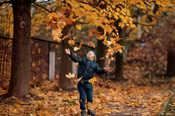 A boy in the autumn forest throws leaves and rejoices