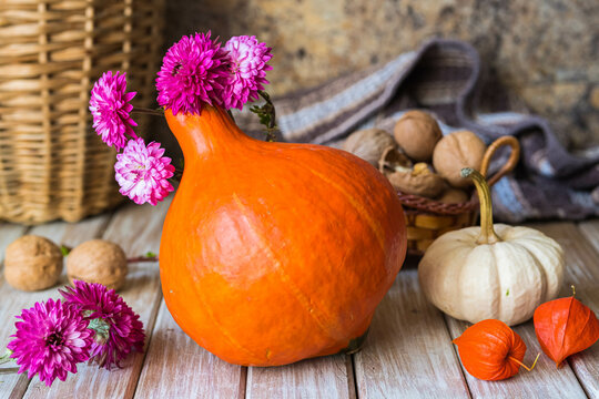 Autumn composition with orange and white pumpkins, flowers and walnuts on a light wooden background. Home decor