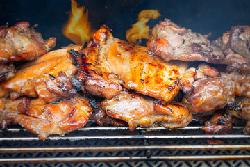 Flames lick teriyaki chicken stacked up on a grill